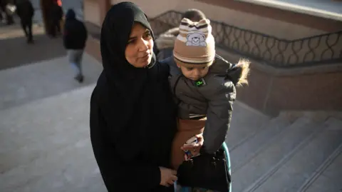 EPA-EFE/REX/Shutterstock A Palestinian woman wearing a black abaya carrying a child walks up the stairs. 