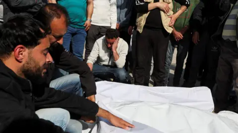 Reuters Mourners cry over the covered bodies of Palestinians killed in Israeli strikes, at Al-Aqsa Martyrs hospital, in Deir Al-Balah on March 18, 2025