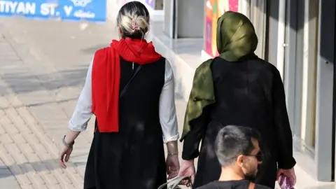 EPA An Iranian woman without a mandatory headscarf, or hijab, walks in a street in Tehran, with another woman who is wearing a hijab.